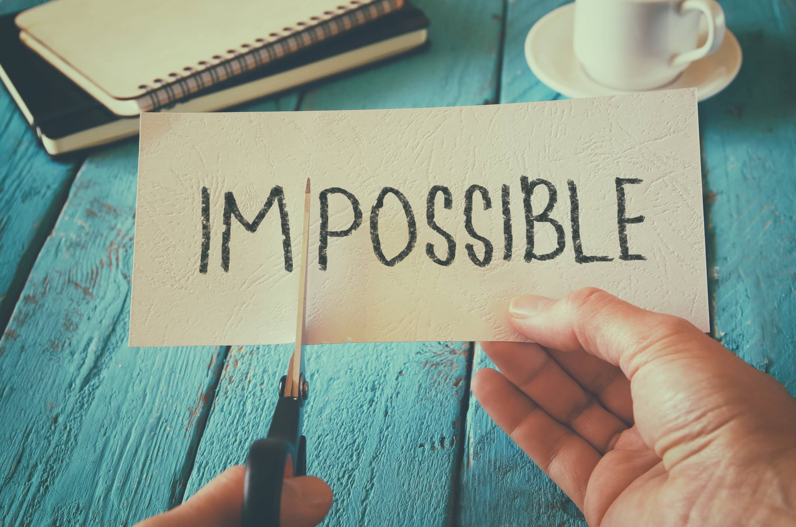 Someone cutting the letters IM from the word IMPOSSIBLE to create POSSIBLE