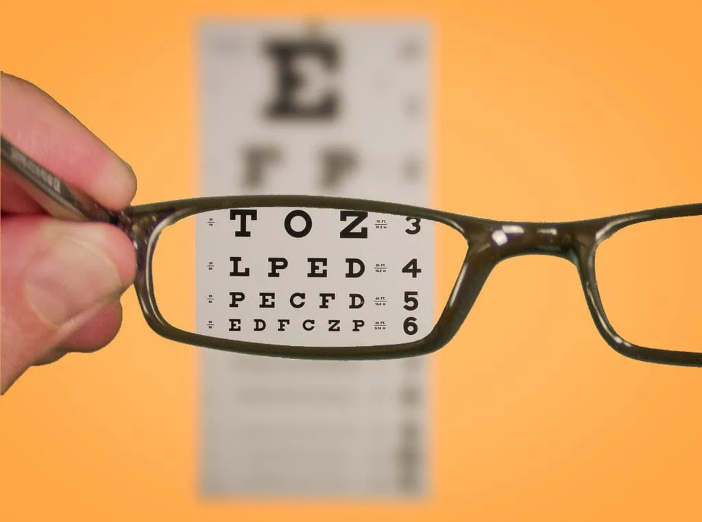 person holding up eye glasses to read blurry eye chart and seeing clearly